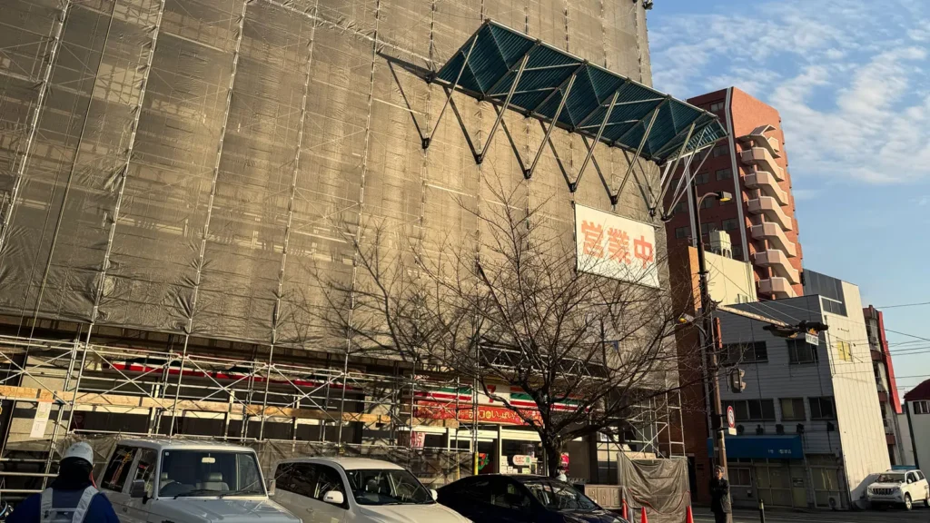 Exterior scaffolding with protective sheeting installed for a building renovation project in Japan, showing a temporary working platform and scaffold structure.