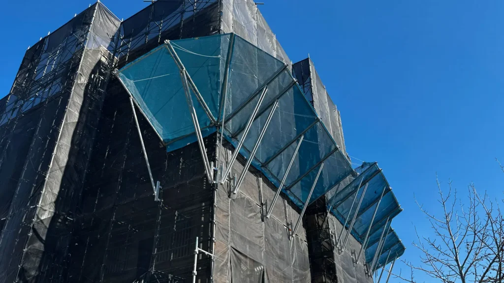 Facade scaffold with debris protection fans installed around a residential building, illustrating details that should be represented in scaffold section drawings.