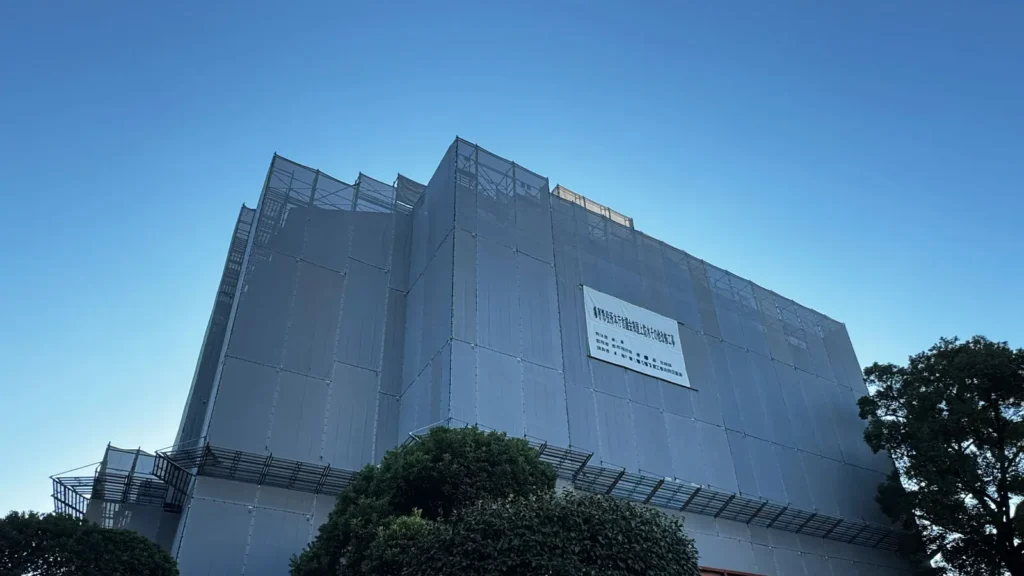 Large building renovation in Japan enclosed with scaffold sheeting, demonstrating a full scaffolding system used for exterior maintenance and safe construction work.