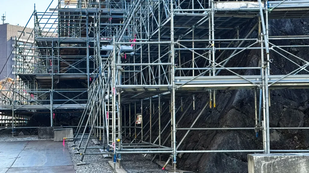 Real scaffold erected beside a rock face showing complex site geometry, bracing, platforms and varying support conditions.