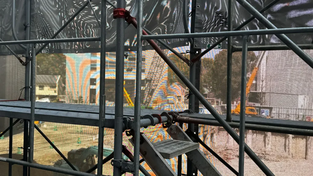 Scaffold bracing with diagonal members, vertical standards, guardrails and connections inside a mesh-covered scaffold