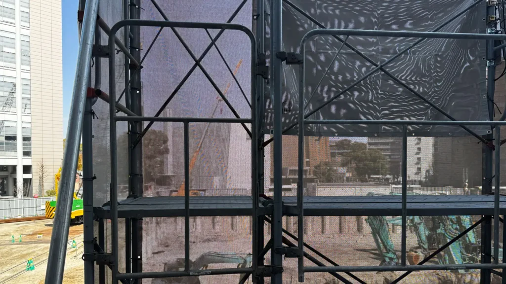 Scaffold bracing layout viewed from inside an erected scaffold with diagonal members, standards, platforms and mesh sheeting
