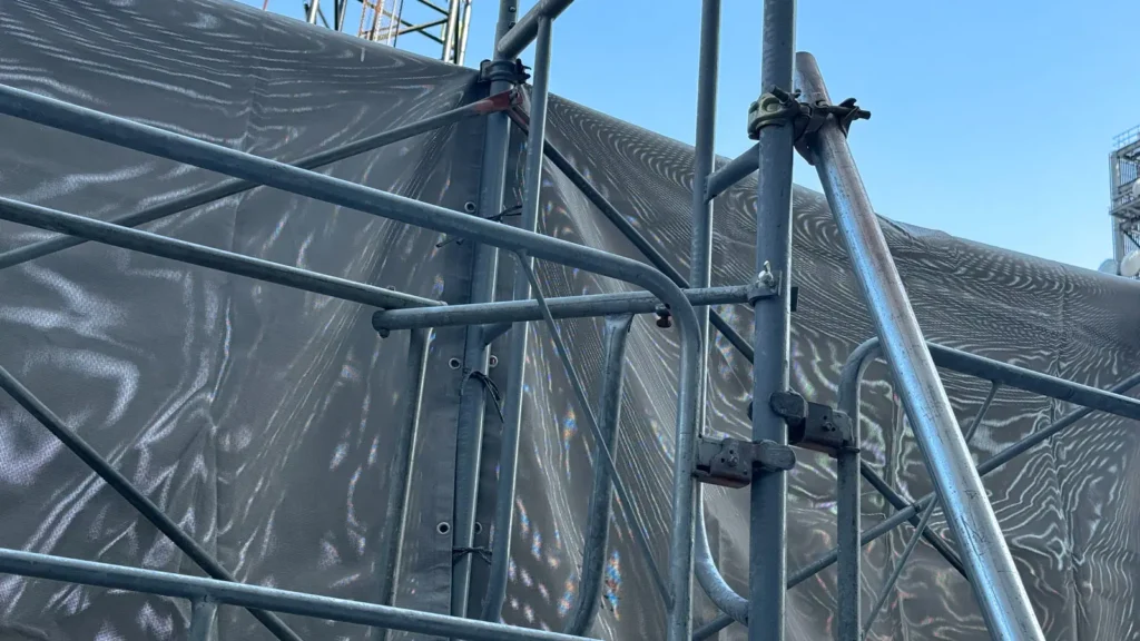 Scaffold bracing and connections installed beside external mesh sheeting on a temporary scaffold structure