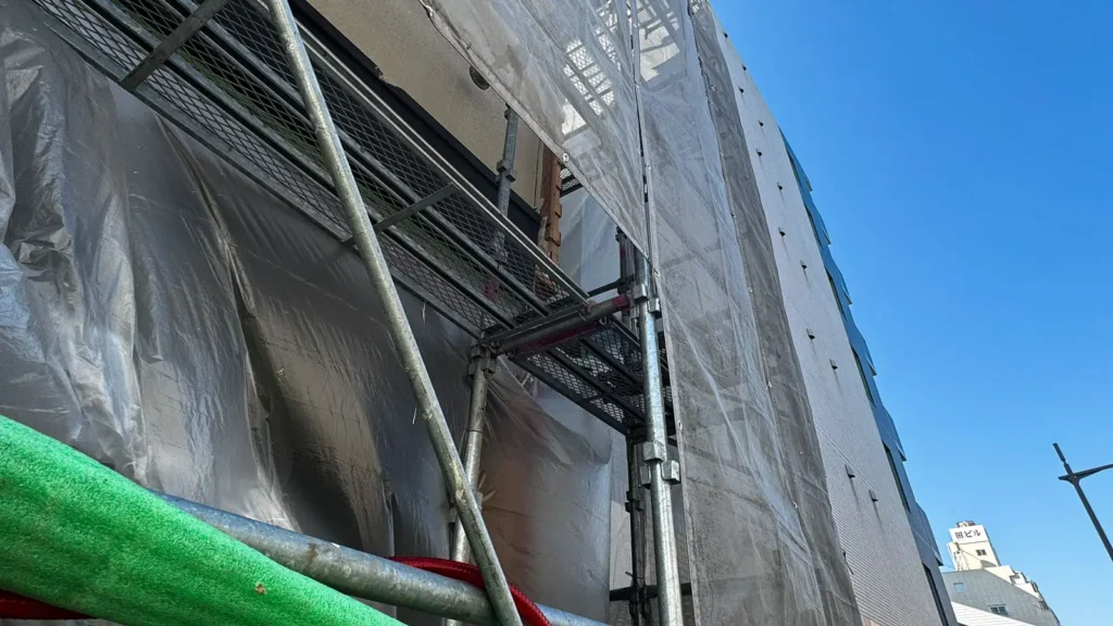 Diagonal scaffold bracing installed beside working platforms and external mesh sheeting on an erected scaffold