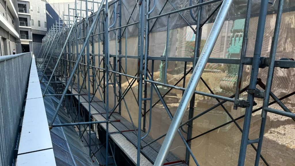 Real scaffold dimensions shown by a long scaffold run with repeated standards, platforms, diagonal bracing and protective mesh.