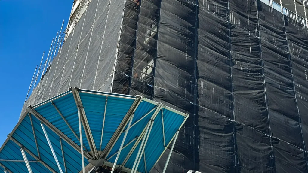 External scaffold covered with black mesh sheeting, illustrating how scaffold enclosure can affect wind loading and tie requirements.