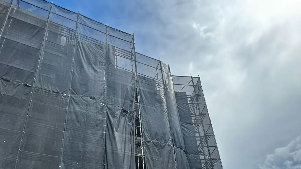 Multi-storey scaffold covered with dark mesh sheeting under exposed weather conditions