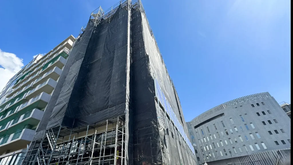 Multi-storey building surrounded by scaffold and protective sheeting during construction work.