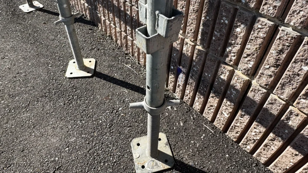 Scaffold base plates supporting adjustable bases on an asphalt surface