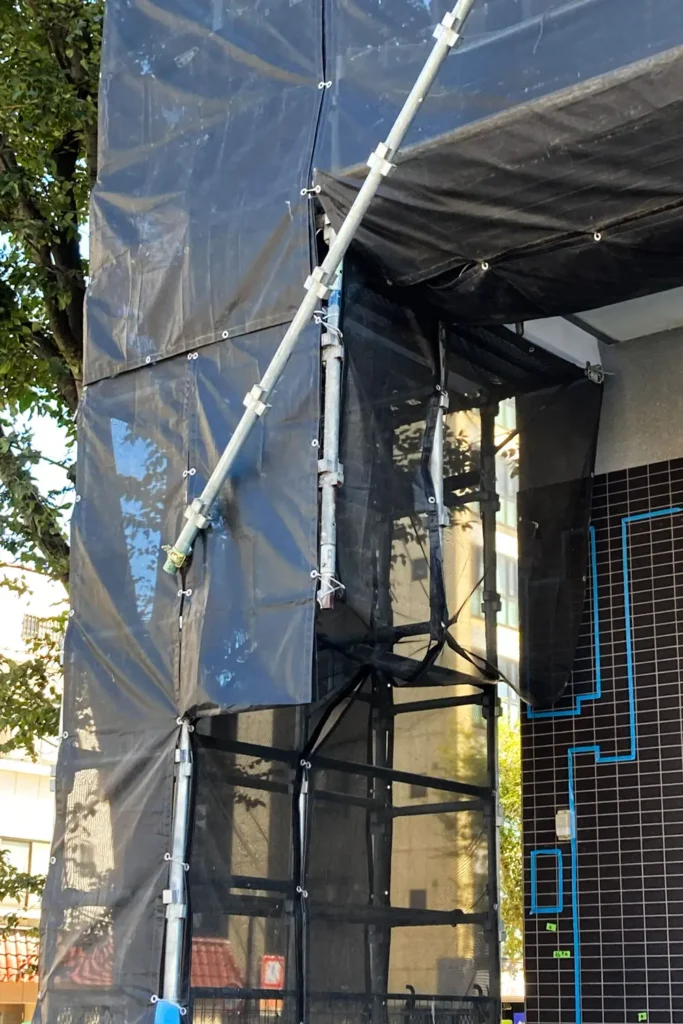 Diagonal scaffold bracing beside a building opening with mesh sheeting