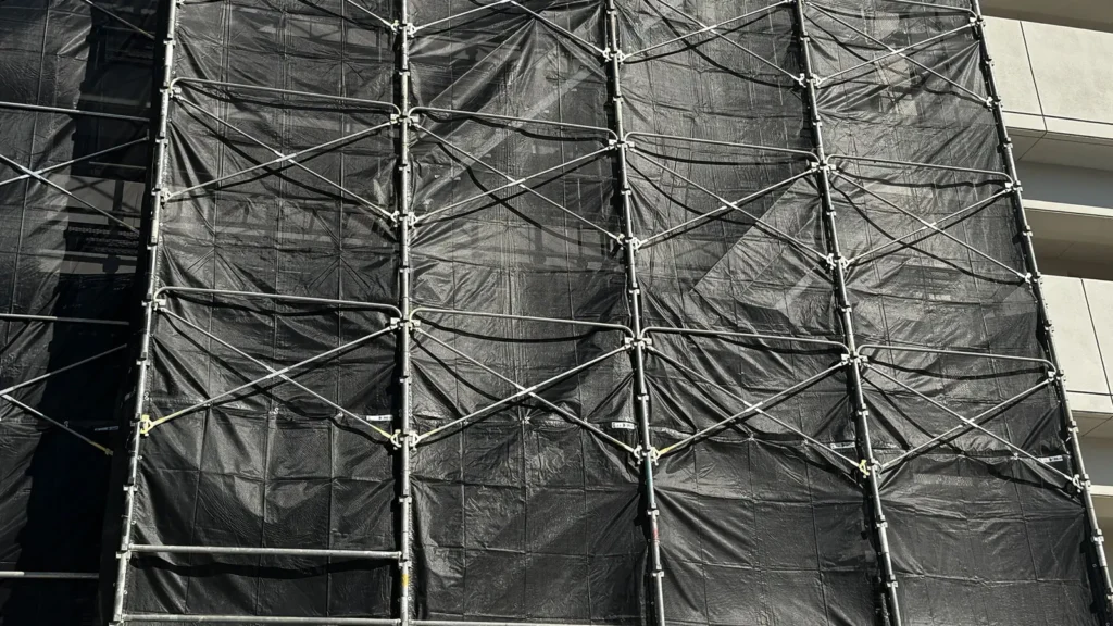 Scaffold with diagonal bracing and black mesh sheeting installed across the exterior