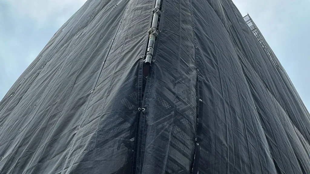 Scaffold covered with dark mesh sheeting showing an enclosed scaffold surface exposed to wind