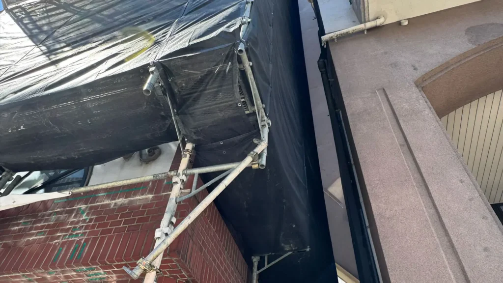 Scaffold positioned in a narrow gap beside a building, showing limited clearance and surrounding building constraints