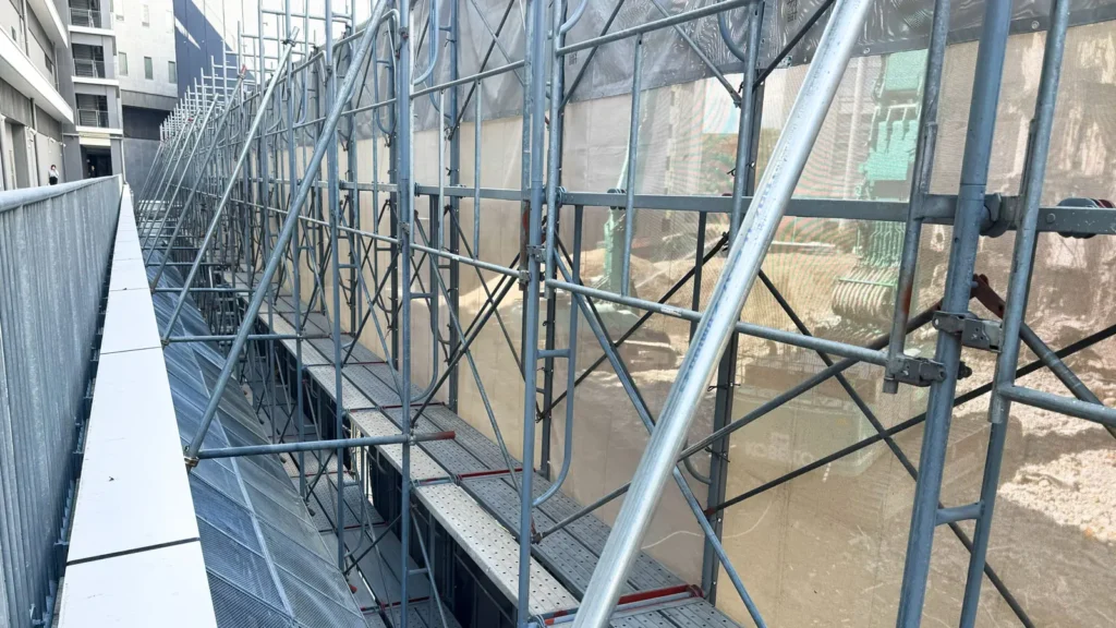Scaffold working platforms and bracing beside a building showing site conditions to review after drawing revisions